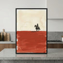 Framed artwork of a cowboy on horseback set against a stark desert landscape with a beige sky and deep red foreground, displayed on a modern kitchen island. The western-style illustration uses bold, minimalist brushstrokes to emphasize solitude and open space.