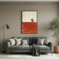 Western-themed painting of a cowboy riding a horse across a red desert, hanging above a modern gray sofa in a neutral-toned living room. The art contrasts a pale sky with a bold rust-colored terrain, adding a rustic yet contemporary touch to the decor.