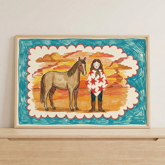 Framed art print of a girl and horse against a vibrant sunset, propped on a light wood shelf with neutral wall tones. The colorful and rustic wall art brings a playful, storybook feel to modern interiors.