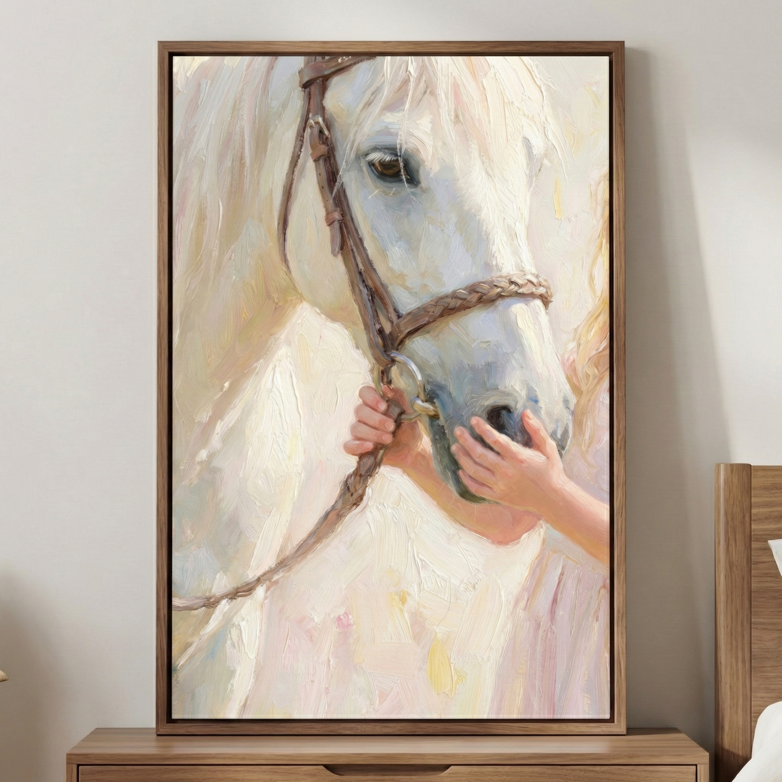 An impressionistic artwork depicting a close-up of a white horse. Thick, visible texture creates the form of the horse's head and its gentle brown eye. A person's small hands reach up to touch the horse's muzzle and hold a leather strap. The color palette is composed of soft whites, creams, and pale pinks. The canvas is housed in a simple wooden frame and displayed on a wooden surface against a neutral wall.