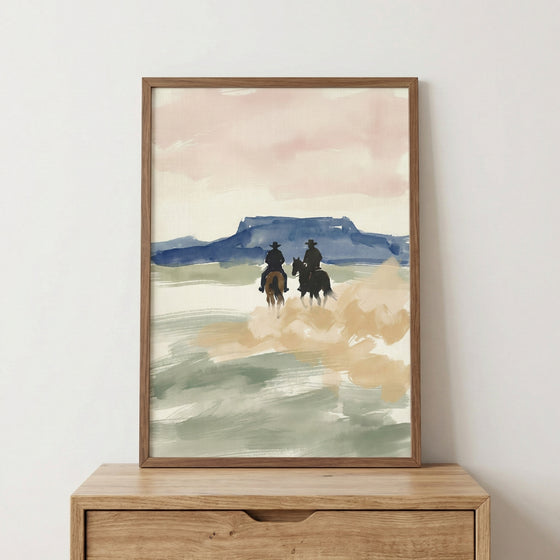 Framed watercolor painting of two cowboys riding horses through an open desert landscape, with soft pastel skies and distant blue mesas. The loose brushstrokes and earthy tones evoke a peaceful western scene.