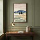 Western-themed art print of two cowboys on horseback kicking up dust as they ride toward a mesa under a pink and blue sky, displayed above a classic wooden desk. The painting captures the quiet motion of a horseback journey through the open range.