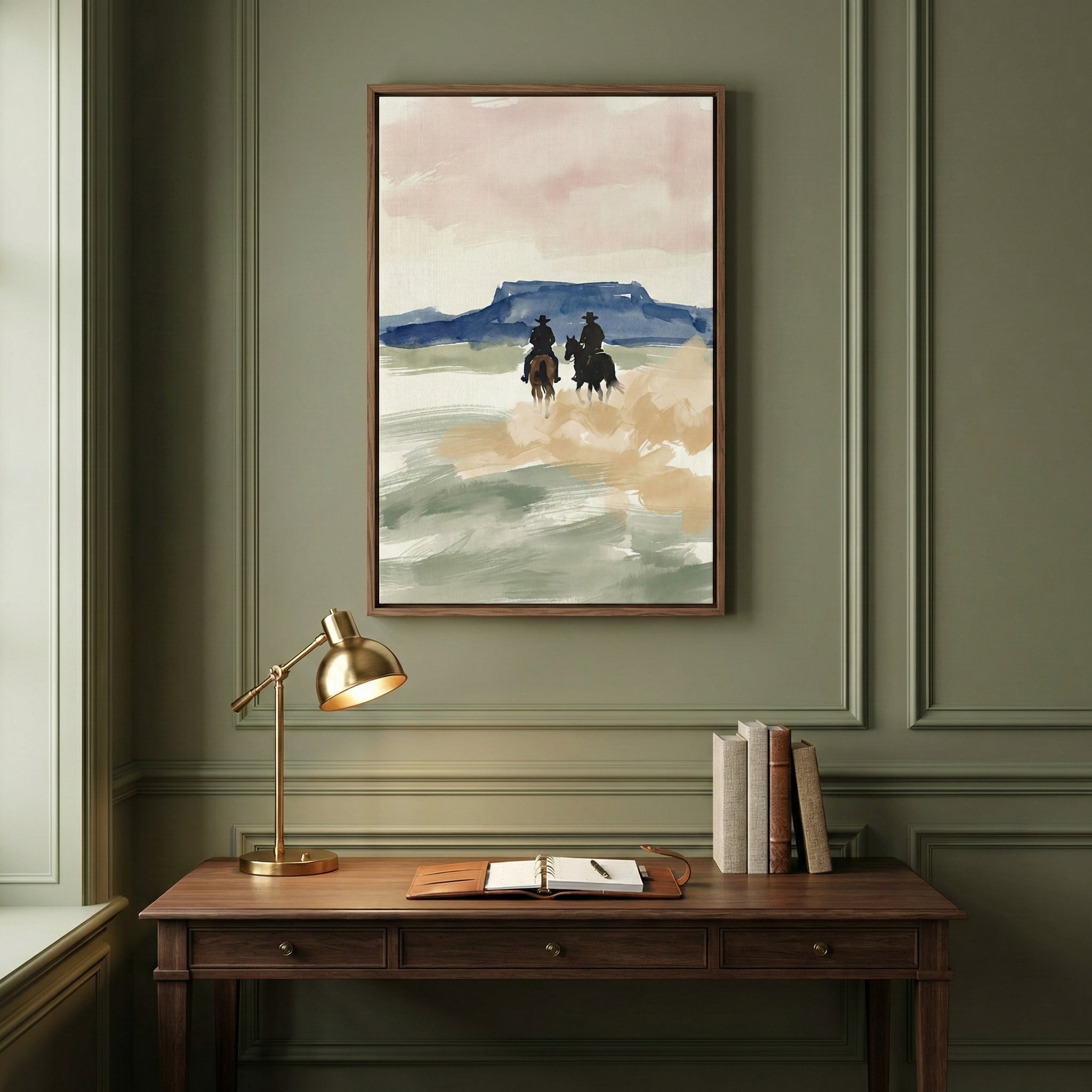 Western-themed art print of two cowboys on horseback kicking up dust as they ride toward a mesa under a pink and blue sky, displayed above a classic wooden desk. The painting captures the quiet motion of a horseback journey through the open range.