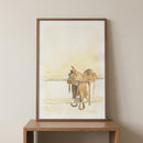 Framed watercolor-style artwork of a western horse saddle resting on a wooden rail, rendered in soft beige and brown tones. The minimalist composition emphasizes the iconic silhouette of cowboy gear against a light, sunlit background.