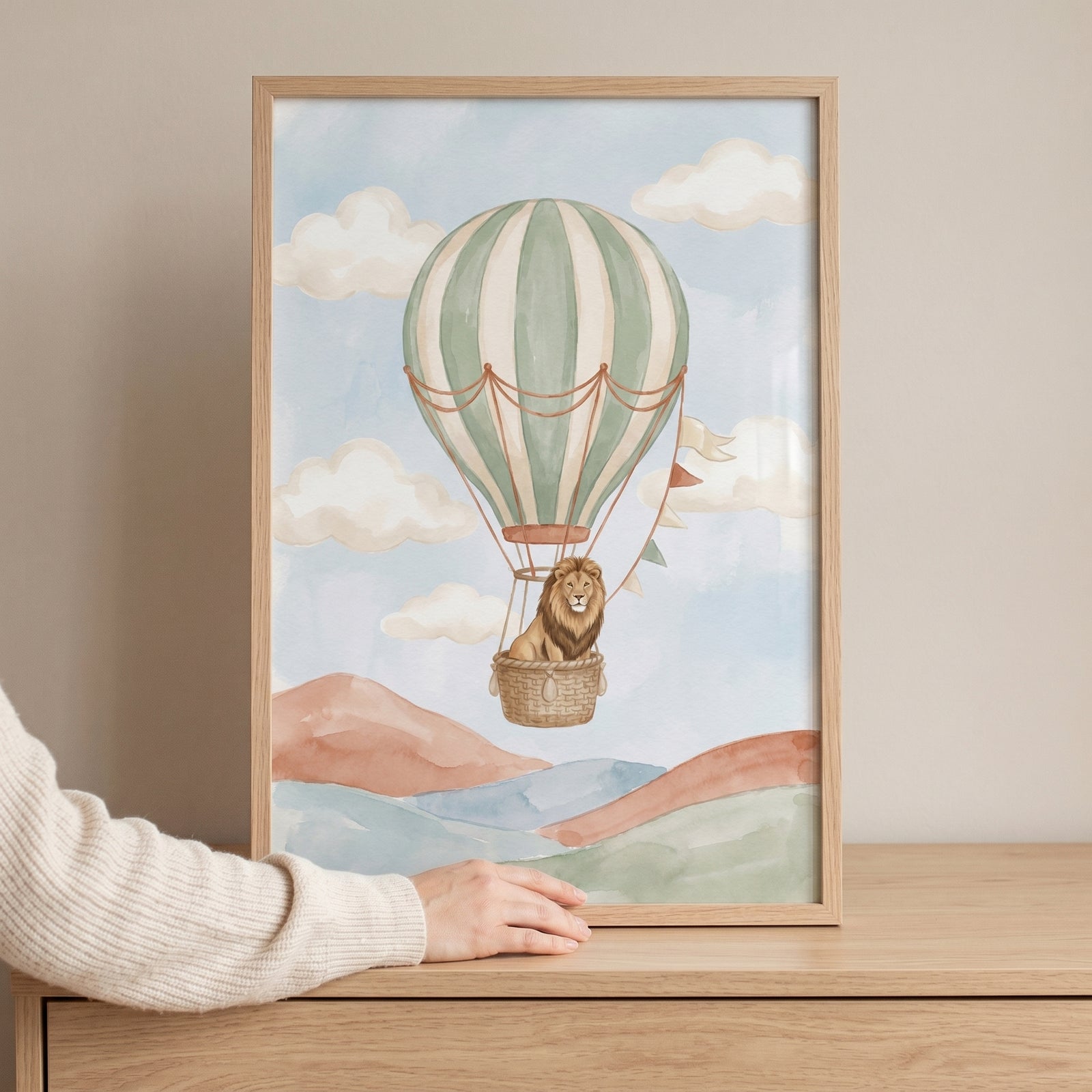 Hot air balloon lion wall art in a wood frame shows a lion in a striped balloon over watercolor hills and clouds.