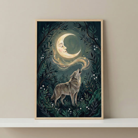 A vertical, wood-framed illustration depicts a wolf in a dark, mystical forest, howling toward a crescent moon that features a peaceful human face. A shimmering trail of golden starlight connects the wolf's howl to the moon. The forest background is filled with layered green foliage and tiny white flowers. The framed piece is displayed on a white shelf against a plain, neutral-toned wall.