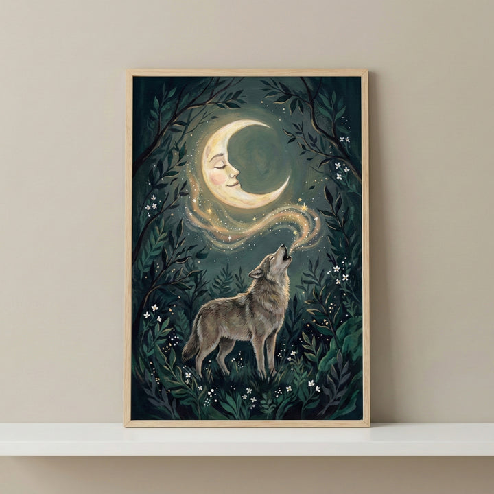 A vertical, wood-framed illustration depicts a wolf in a dark, mystical forest, howling toward a crescent moon that features a peaceful human face. A shimmering trail of golden starlight connects the wolf's howl to the moon. The forest background is filled with layered green foliage and tiny white flowers. The framed piece is displayed on a white shelf against a plain, neutral-toned wall.