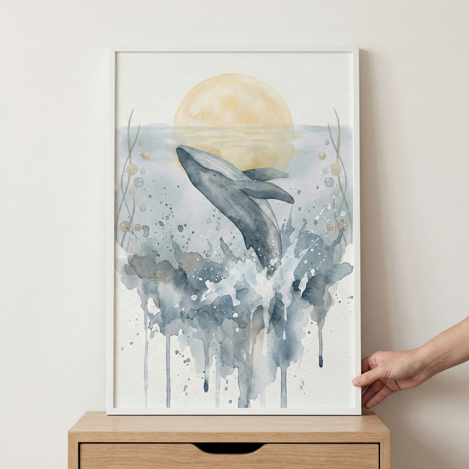 This vertical watercolor artwork showcases a majestic whale leaping out of a splashing sea. The whale is rendered in shades of dark gray and deep blue, its body arched as it breaches the water's surface. Below it, expressive washes of blue and gray water form energetic splashes and drips that flow down the composition. In the center background, a large, soft pale-yellow circle representing a sun or moon sits low on the horizon, casting a gentle glow. 