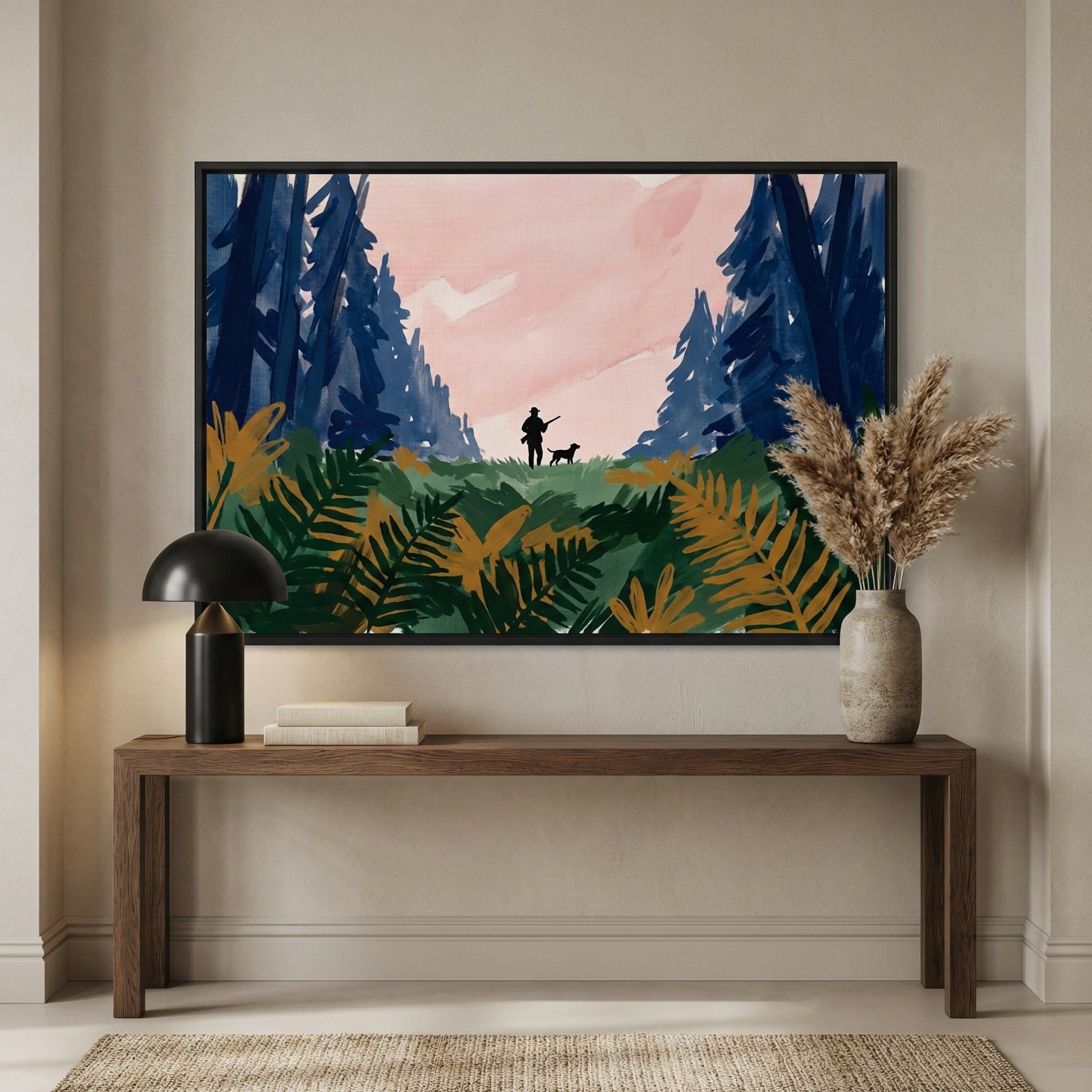 A large framed landscape artwork hangs centered on a neutral-toned wall above a long, minimalist wooden console table. The artwork depicts a stylized outdoor scene with broad, expressive strokes. In the distant center, a silhouette of a person and a dog stand in a clearing, framed by tall, dark blue coniferous trees under a soft pink sky. The foreground of the piece features vibrant, oversized foliage in shades of deep green and warm amber.