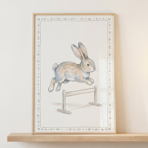 Watercolor hurdle rabbit wall art of a brown rabbit leaping over a small hurdle, displayed in a light wood frame.