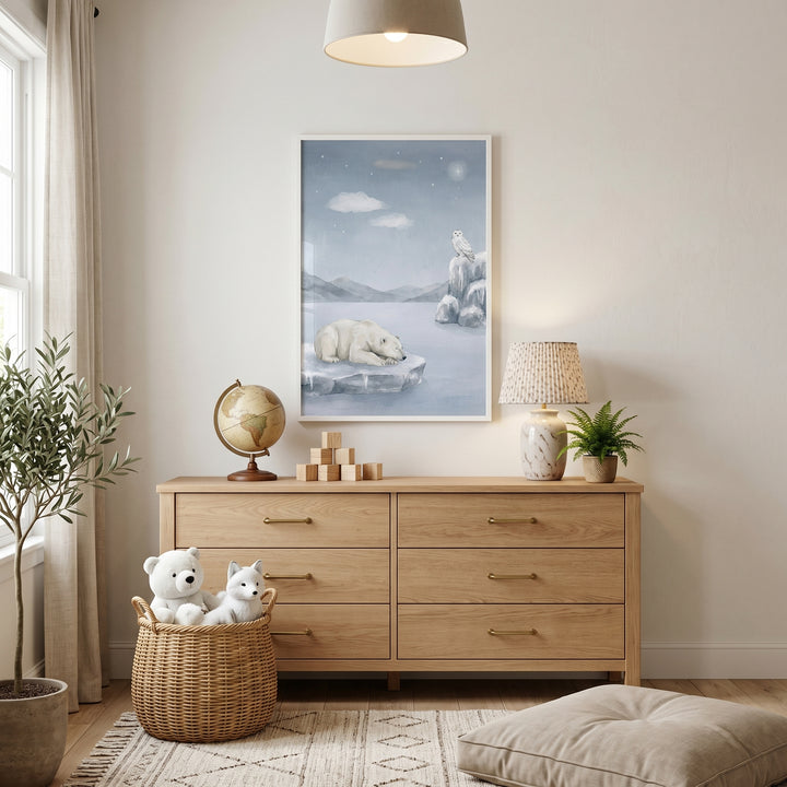 Ice floe polar bear wall art hangs above a wooden dresser in a room with a globe, lamp, and plush-filled wicker basket.