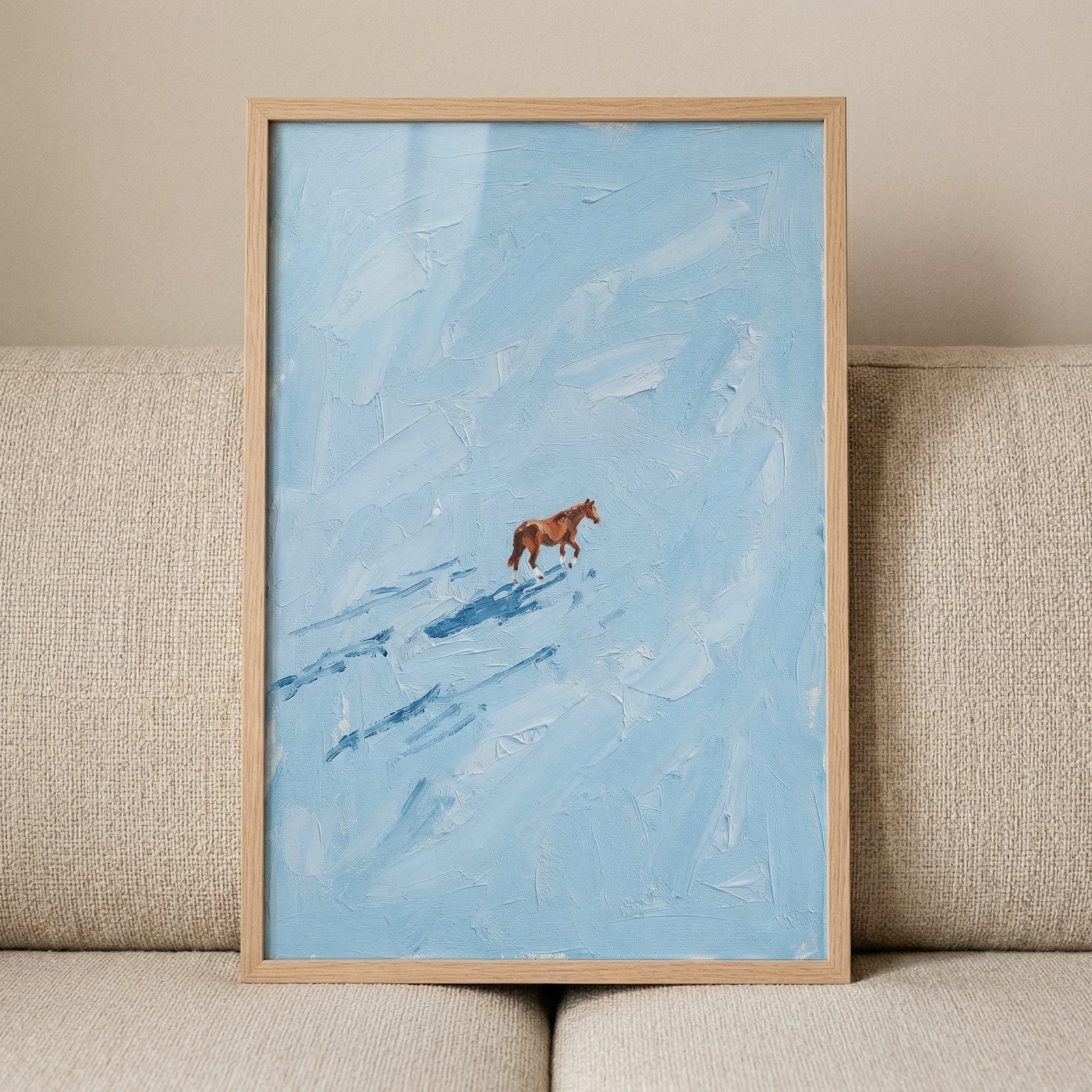 A framed piece of artwork depicting a solitary brown horse walking across an expansive, textured light blue field. The blue background is rendered with thick, visible strokes, creating a sense of movement and depth reminiscent of windswept snow. 