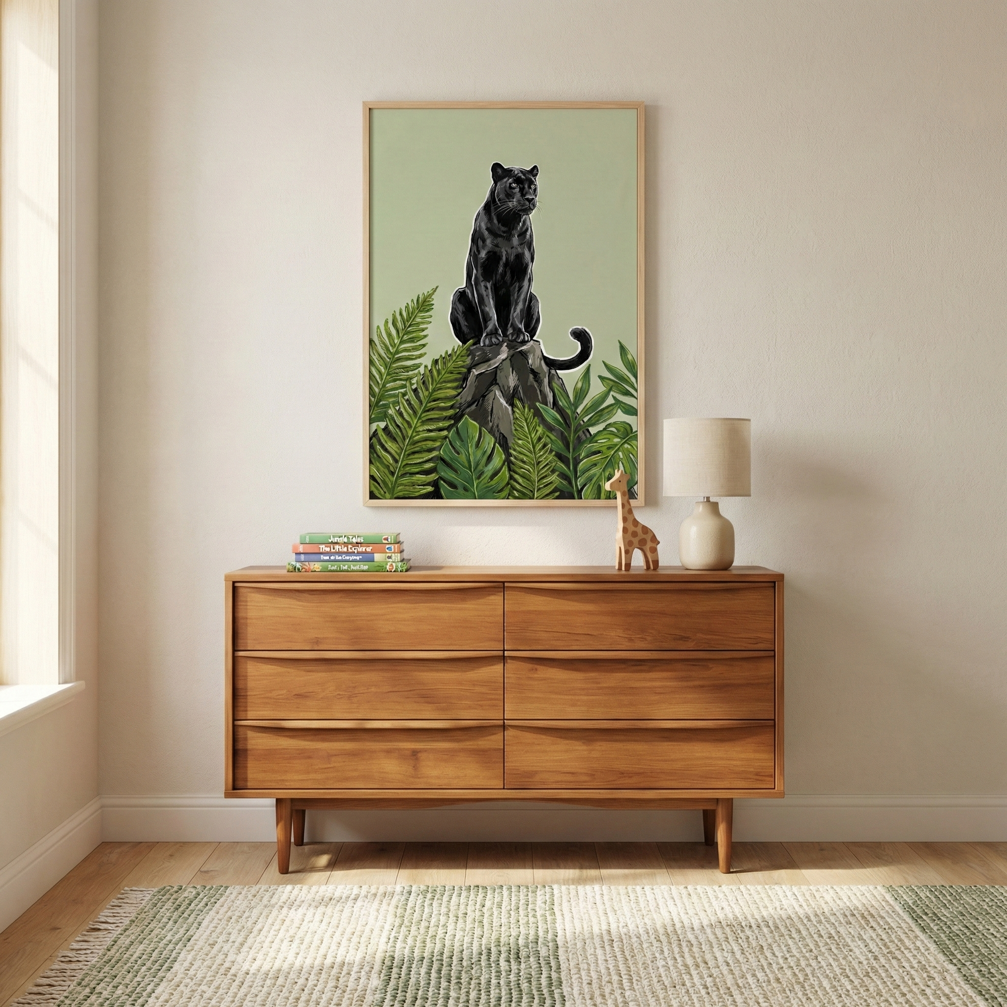 A wooden dresser with a mid-century design stands against a light-colored wall, topped with a stack of books, a small giraffe figurine, and a beige lamp. Above it hangs a framed artwork of a black panther perched on a rock surrounded by lush green leaves.