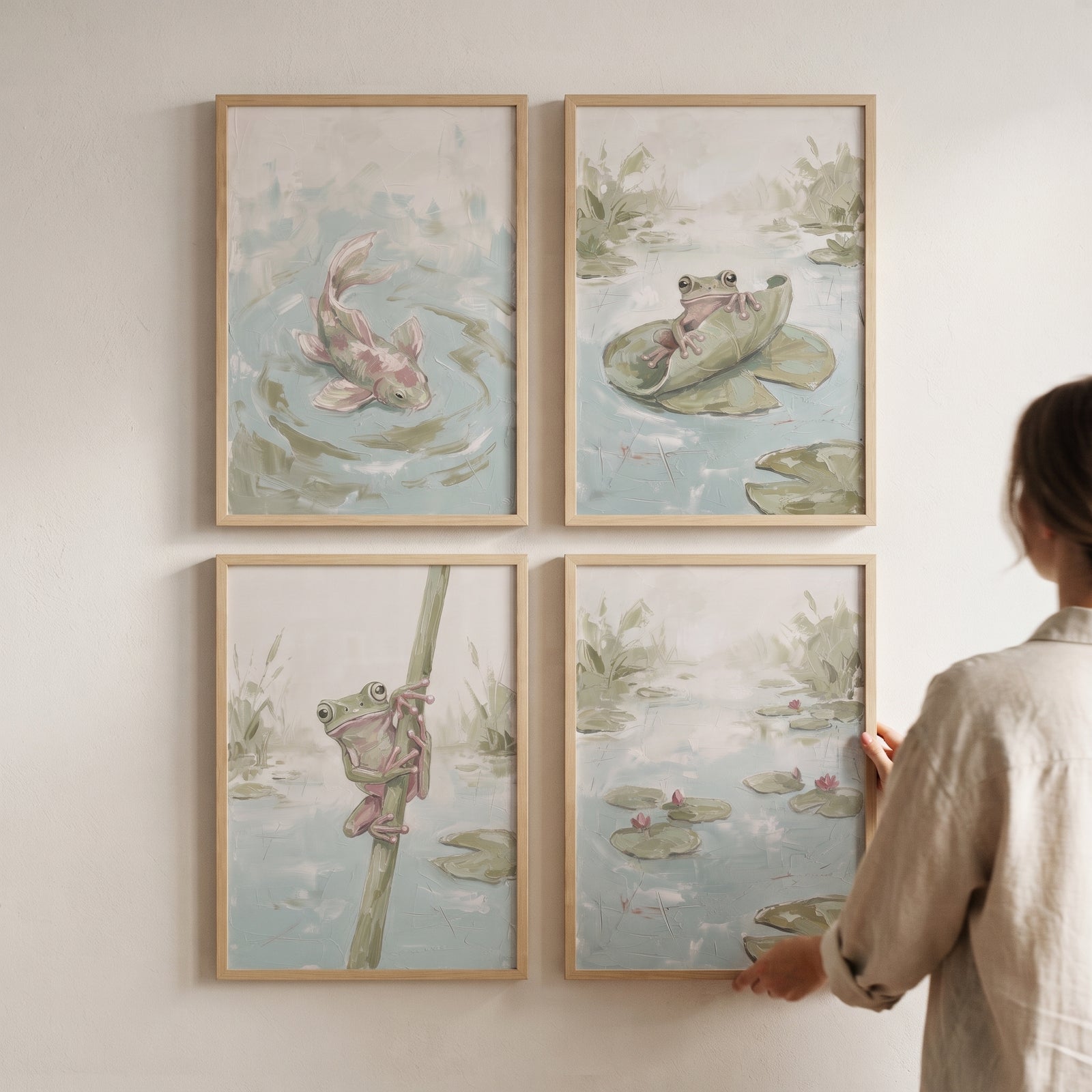 A person adjusts an impasto sage marsh animals wall art set of 4 featuring frogs and a fish on a light wall.