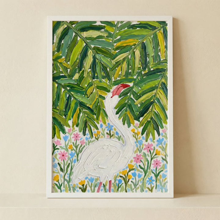 Framed painting of a white bird standing among colorful wildflowers beneath large green tropical leaves. The textured brushstrokes and bright foliage create a lively nature inspired focal point against a neutral wall.