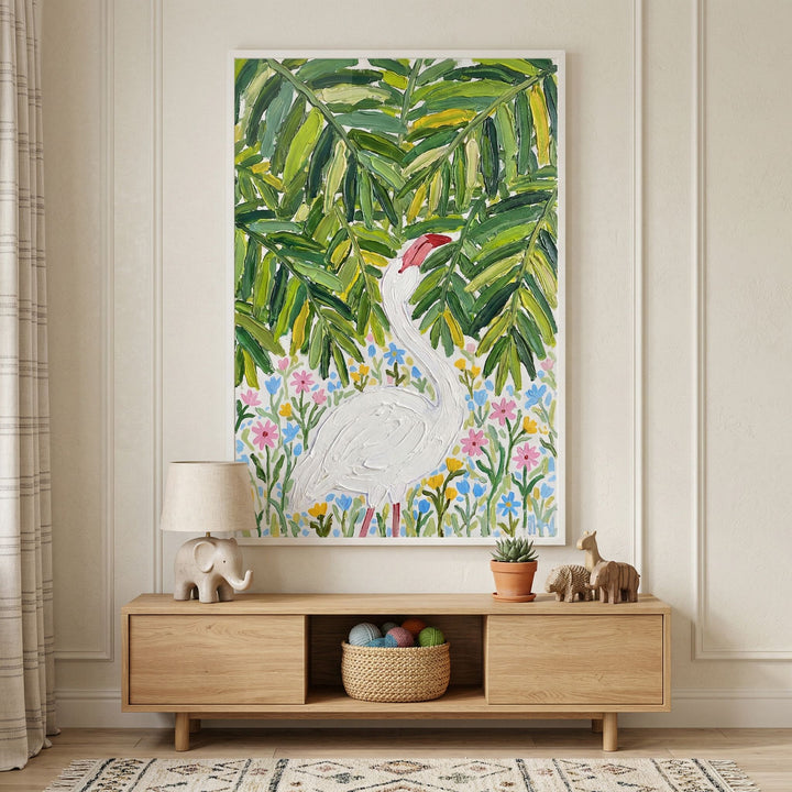 Framed painting of a white bird standing among colorful flowers beneath dense green leaves hangs above a wooden console table styled with a lamp plant and small animal figurines. The neutral wall and soft decor create a calm nature inspired nursery or living space.