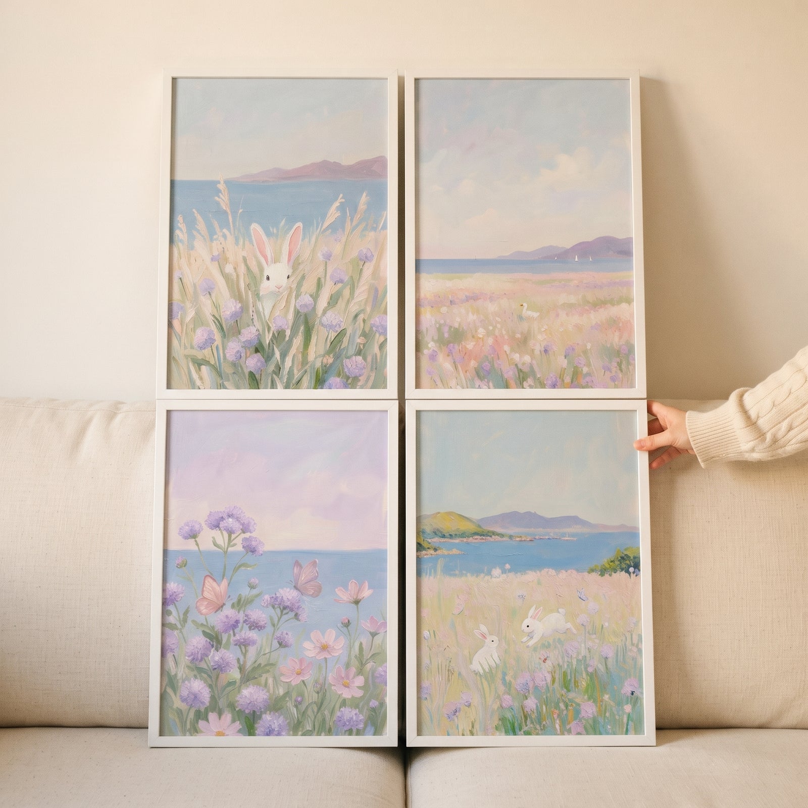 Impressionist lavender coastal wall art set of 4 with bunnies and flowers by the sea in white frames on a couch.