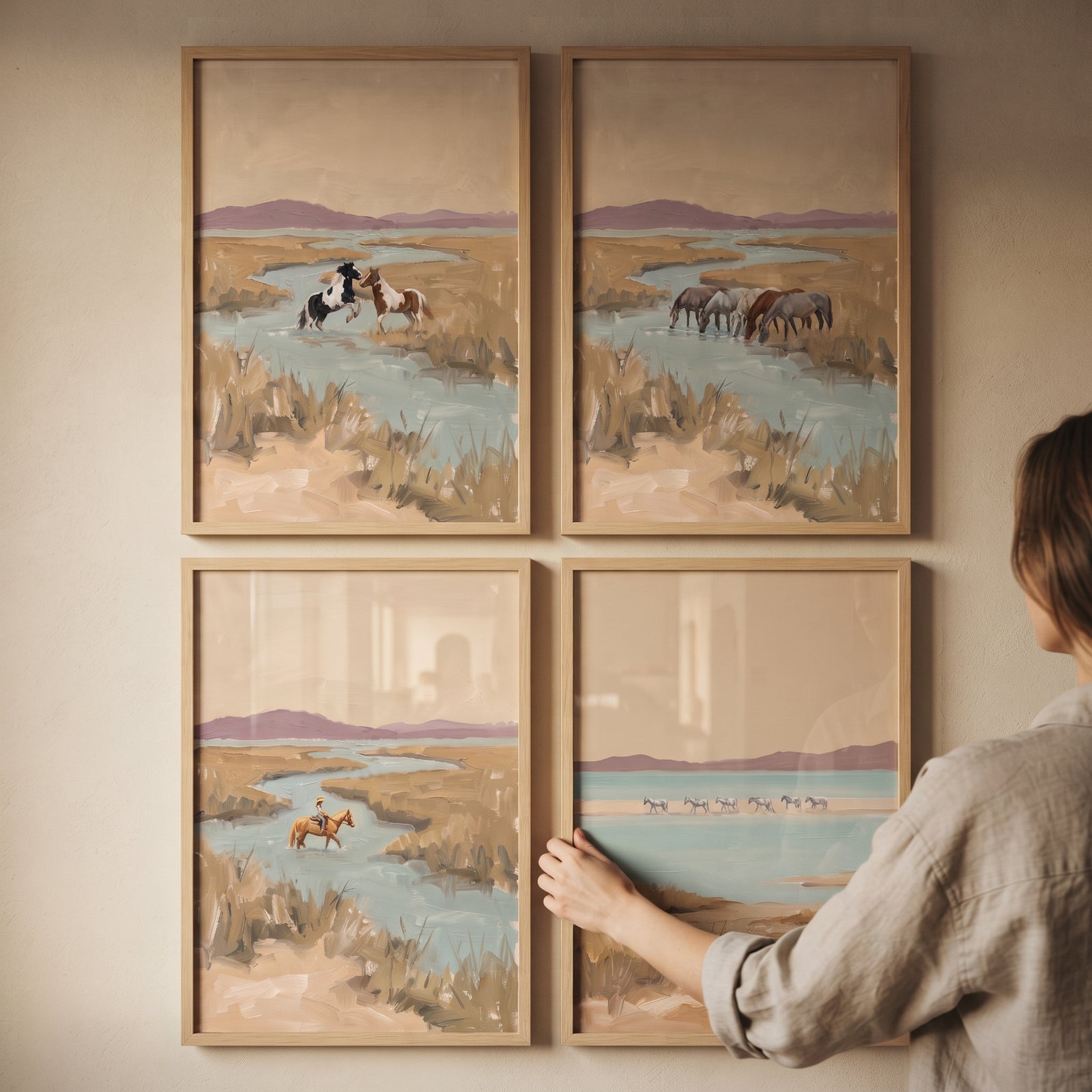 A person hangs an impressionist mauve hills horses wall art set of 4 showing horses and water in a landscape.