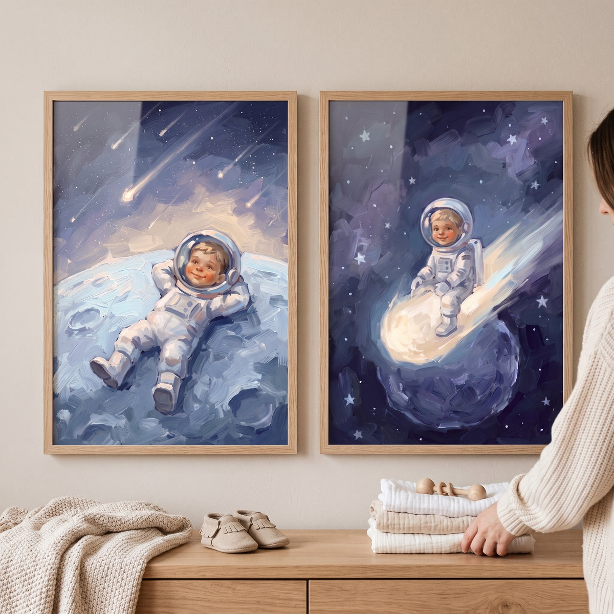 Impressionist sky baby astronaut wall art set of 2 hangs above a wooden dresser with baby shoes and folded blankets.