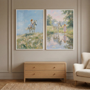 Two framed impressionist paintings hang above a wooden dresser in a neutral room showing a young blonde girl with a white horse in peaceful countryside scenes. One shows the girl riding across a breezy wildflower hill under a blue sky while the other shows her gently leading the horse through a shallow reflective stream surrounded by greenery.