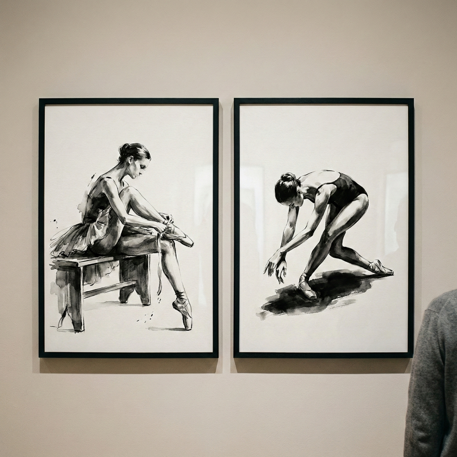 Two monochrome ink-style illustrations of ballerinas are displayed in thin black frames against a neutral wall. In the frame on the left, a ballerina sits on a wooden bench, leaning forward to adjust her pointe shoes while wearing a tutu. In the frame on the right, another dancer in a leotard is depicted in a fluid, leaning pose with arms reaching down, casting a dark shadow on the floor beneath her. A small portion of a person's grey-clad shoulder is visible on the far right.