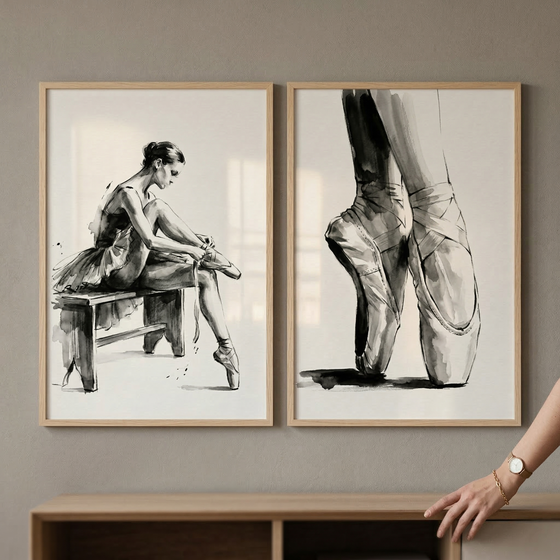 Two light wood-framed ink sketches sit side-by-side on a wooden ledge against a beige wall. The artwork on the left depicts a ballerina sitting on a bench, leaning over to tie her pointe shoe. The artwork on the right is a close-up of a dancer's legs and feet standing en pointe. Both illustrations are done in a loose, fluid style with black ink on a white background. A section of a tan, chunky-knit sweater is partially visible on the right edge of the frame.