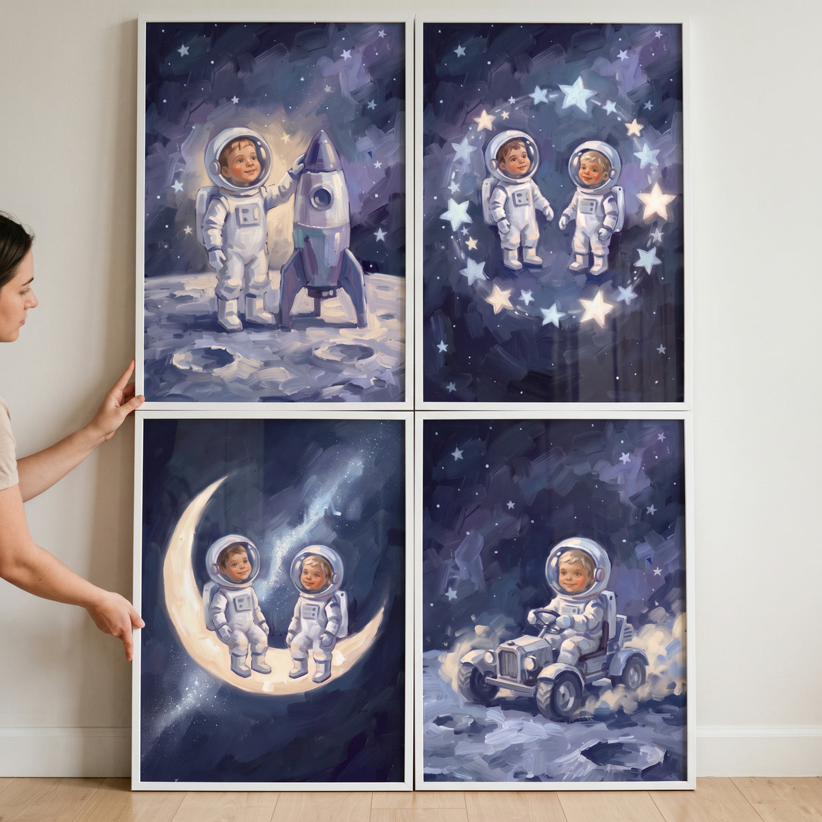 Person holds an inky sapphire baby astronaut wall art set of 4 featuring cosmic illustrations in white frames.