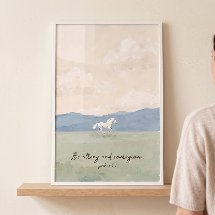 Joshua scripture white horse wall art shows a horse in a field with mountains and text be strong and courageous Joshua 1:9.
