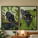 Two framed vertical graphic illustrations hang side-by-side on a light-colored wall above a wooden nightstand. The left piece features a full-bodied black leopard with subtle spots, crouched on a mossy branch while drinking from a pool of water that shows its reflection. The right artwork is a close-up portrait of the big cat’s head with striking yellow eyes, partially hidden behind lush green fern leaves. Below the art, a small lamp and two potted plants sit on a wooden table next to a bed.