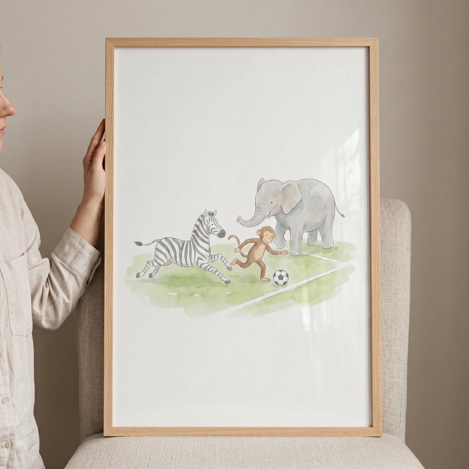Framed watercolor illustration of a zebra, monkey, and elephant kicking ball brown animals wall art on a field.