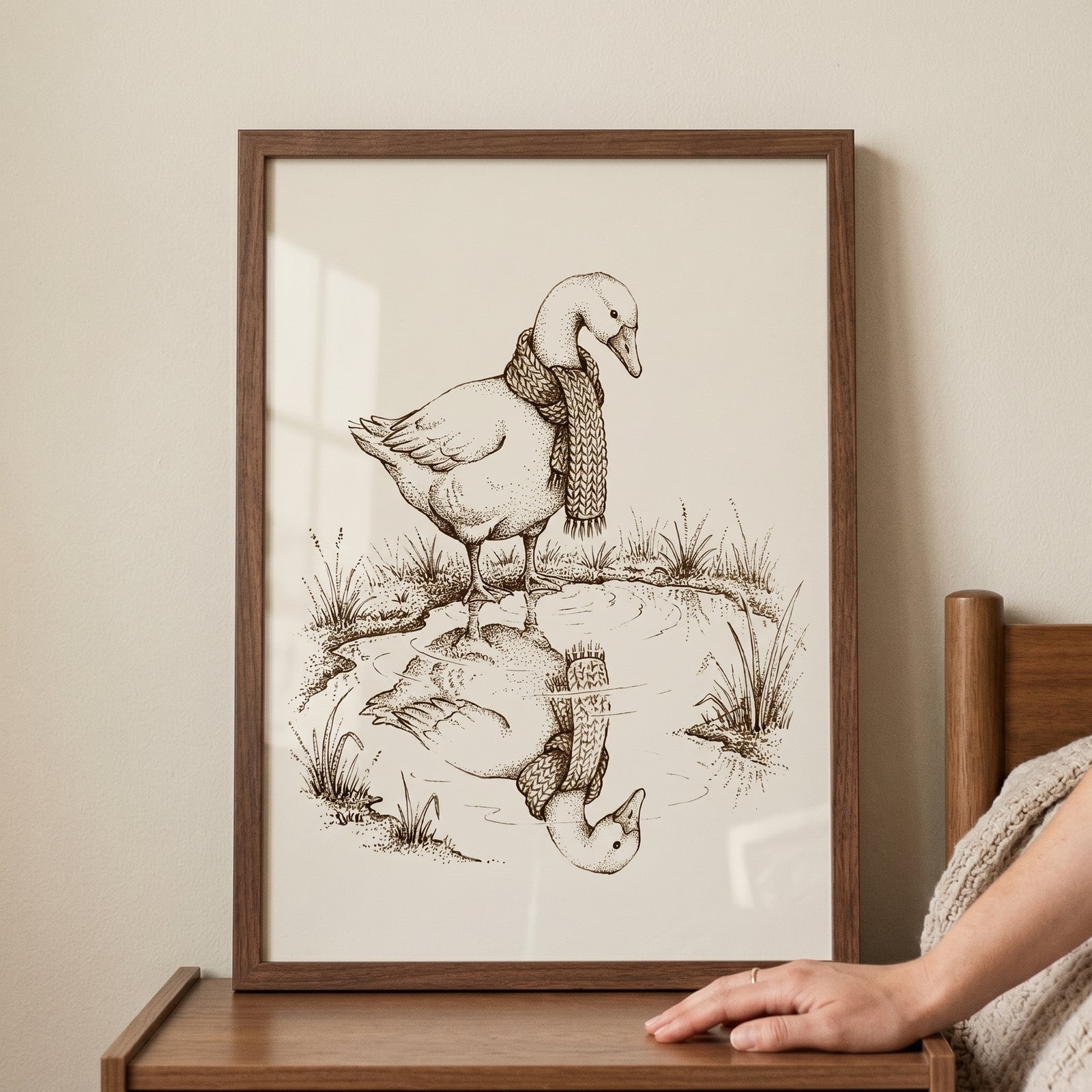 Framed knit scarf reflection goose wall art shows a bird in a scarf looking at its mirrored image in a pond.