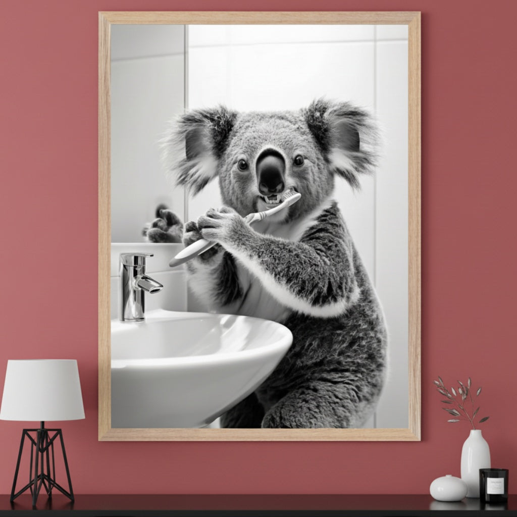 Modern room with a dusty rose wall and a black dresser. A large light wood framed black and white photo of a koala brushing its teeth at a bathroom sink is centered above the dresser. A white lamp and small decor items are on the dresser.