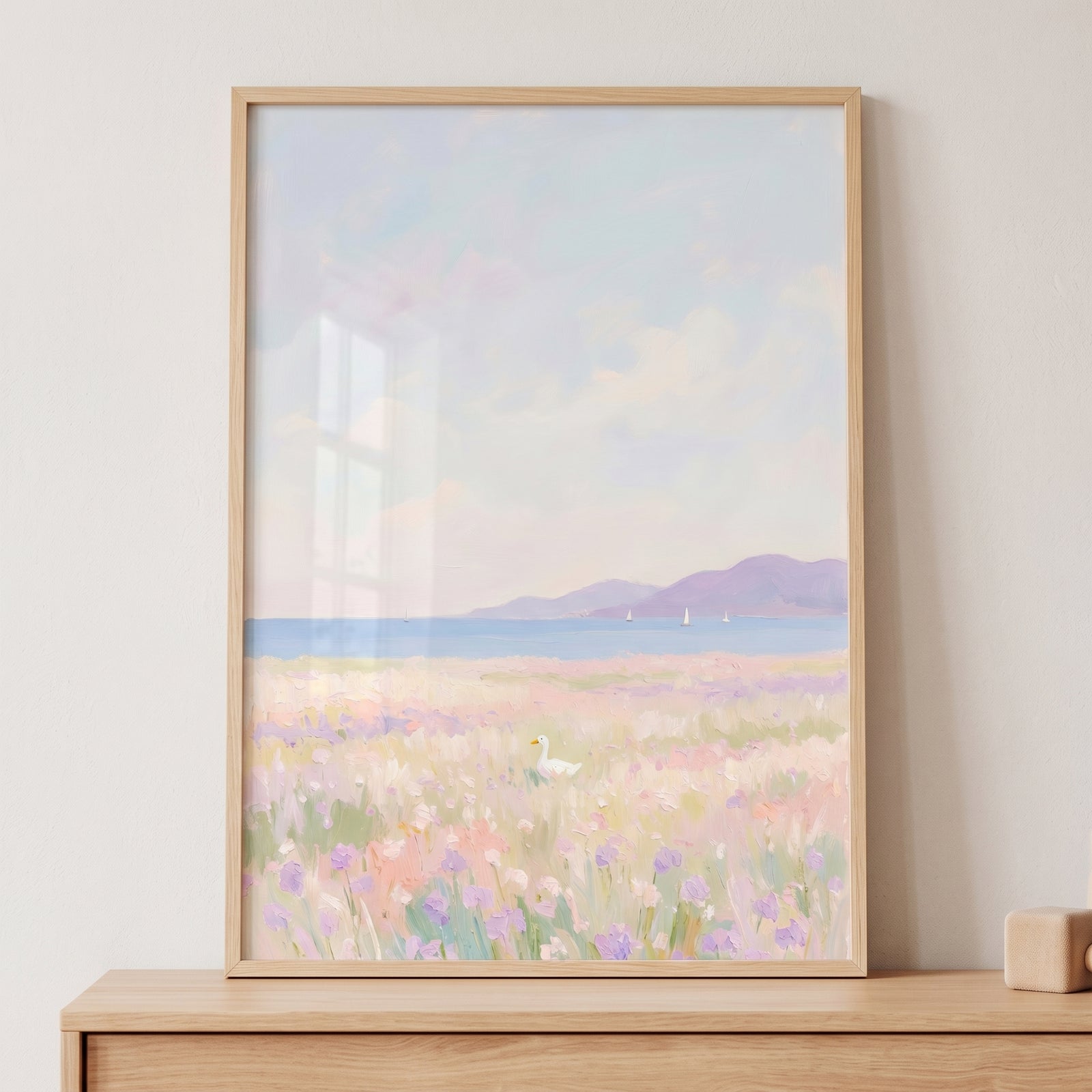 Soft pastel lavender field white duck wall art in a wood frame depicts a wildflower meadow, blue sea, and purple mountains.