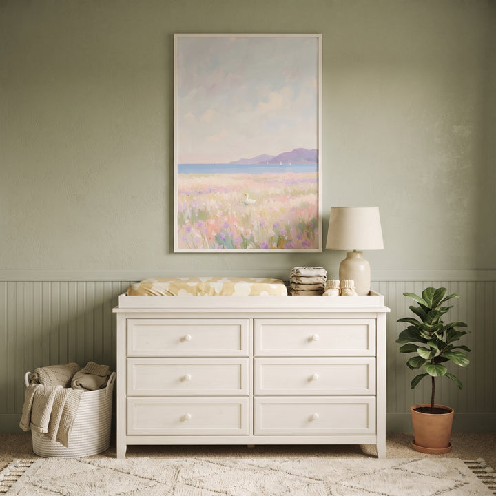 Lavender field white duck wall art hangs above a white dresser in a sage green nursery with a plant and basket.