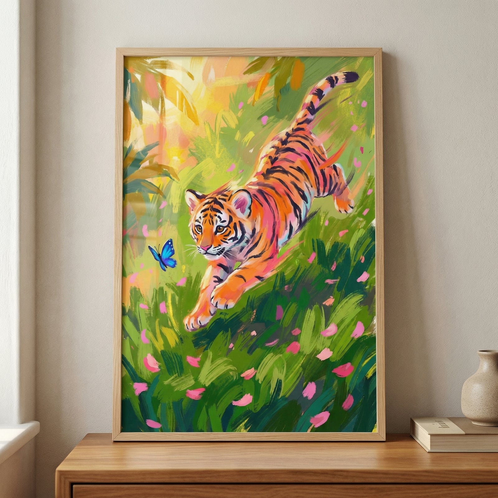 A framed digital illustration features a lively tiger cub leaping through a dense field of green grass and scattered pink petals. The cub's orange fur and black stripes are rendered with expressive, visible strokes that convey a sense of motion and energy. A small, bright blue butterfly flutters in the air just ahead of the cub. 