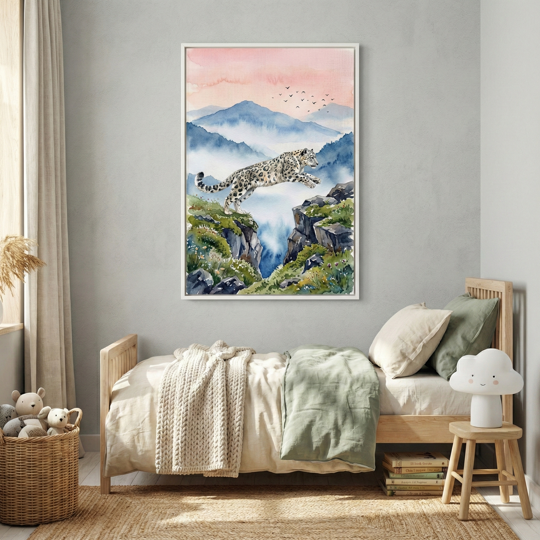 A large, framed artwork of a snow leopard jumping between two rocky cliffs hangs on a gray wall above a child’s bed. The illustration is in a watercolor style, featuring misty blue mountains under a soft pink sunset sky with birds in flight. The wooden bed has neutral-toned bedding. To the side, a cloud-shaped lamp sits on a small stool next to a stack of books. A woven basket filled with soft toys is on the natural fiber rug below, creating a serene and cozy atmosphere.