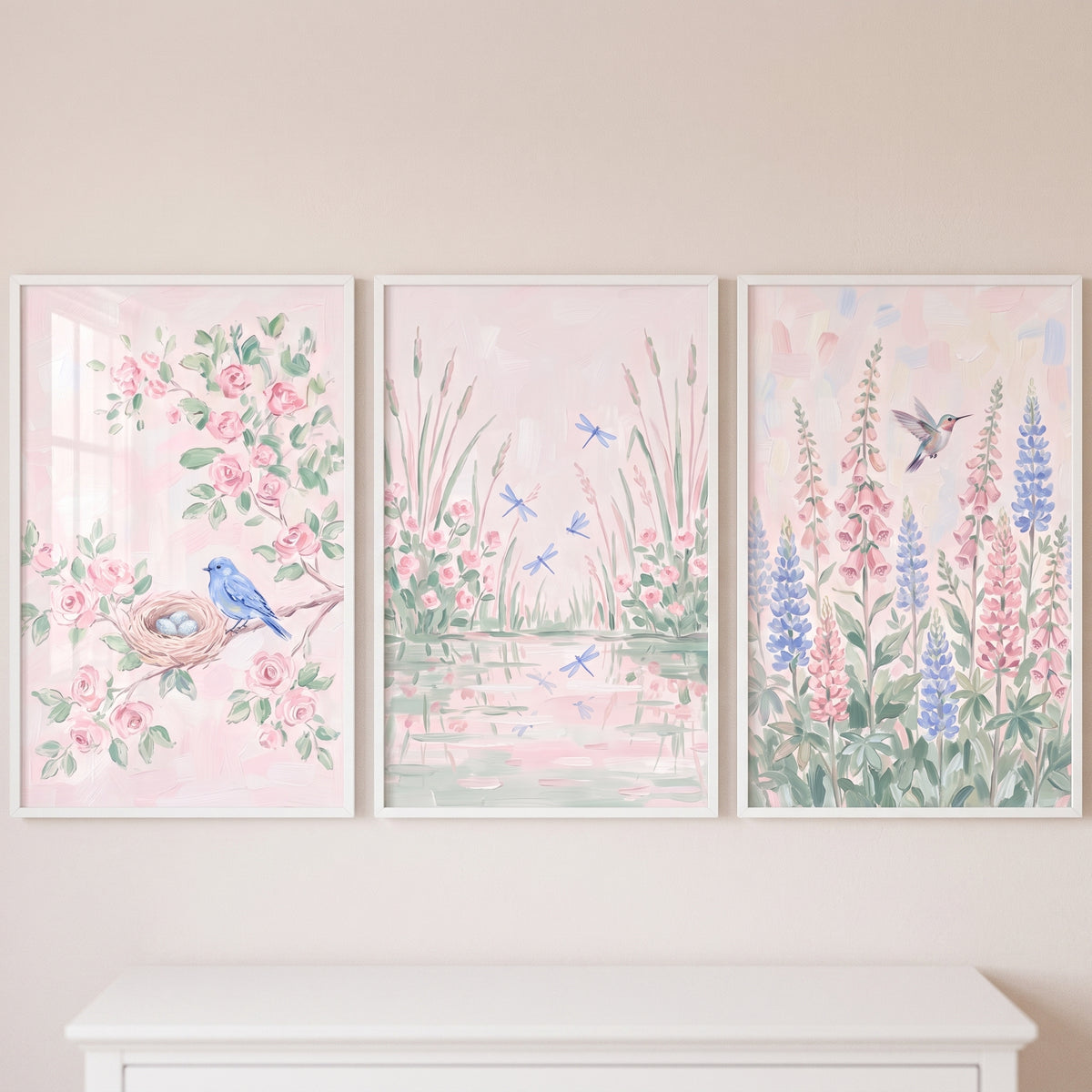 Light pink botanical wall art set of 3 with a bluebird, dragonflies by water, and a hummingbird among tall flowers.