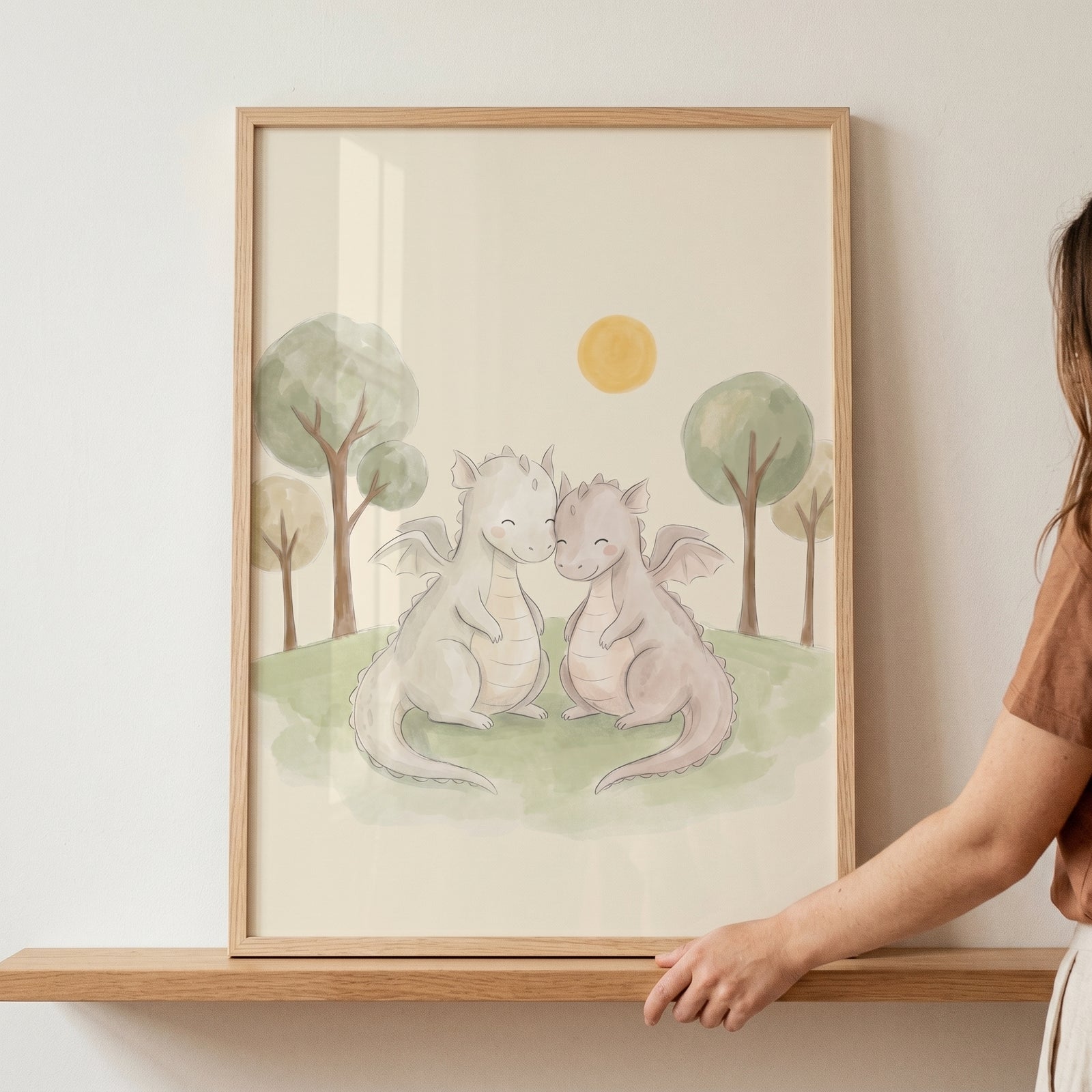 Lilac cream baby dragons wall art in a wooden frame on a shelf shows two dragons in a sunny meadow with trees.