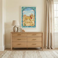 Framed illustration of a cowboy lion in a desert with cacti hangs above a light wood dresser in a neutral-toned room with natural light. The playful desert-themed artwork adds a charming, Western touch to the minimalist decor.