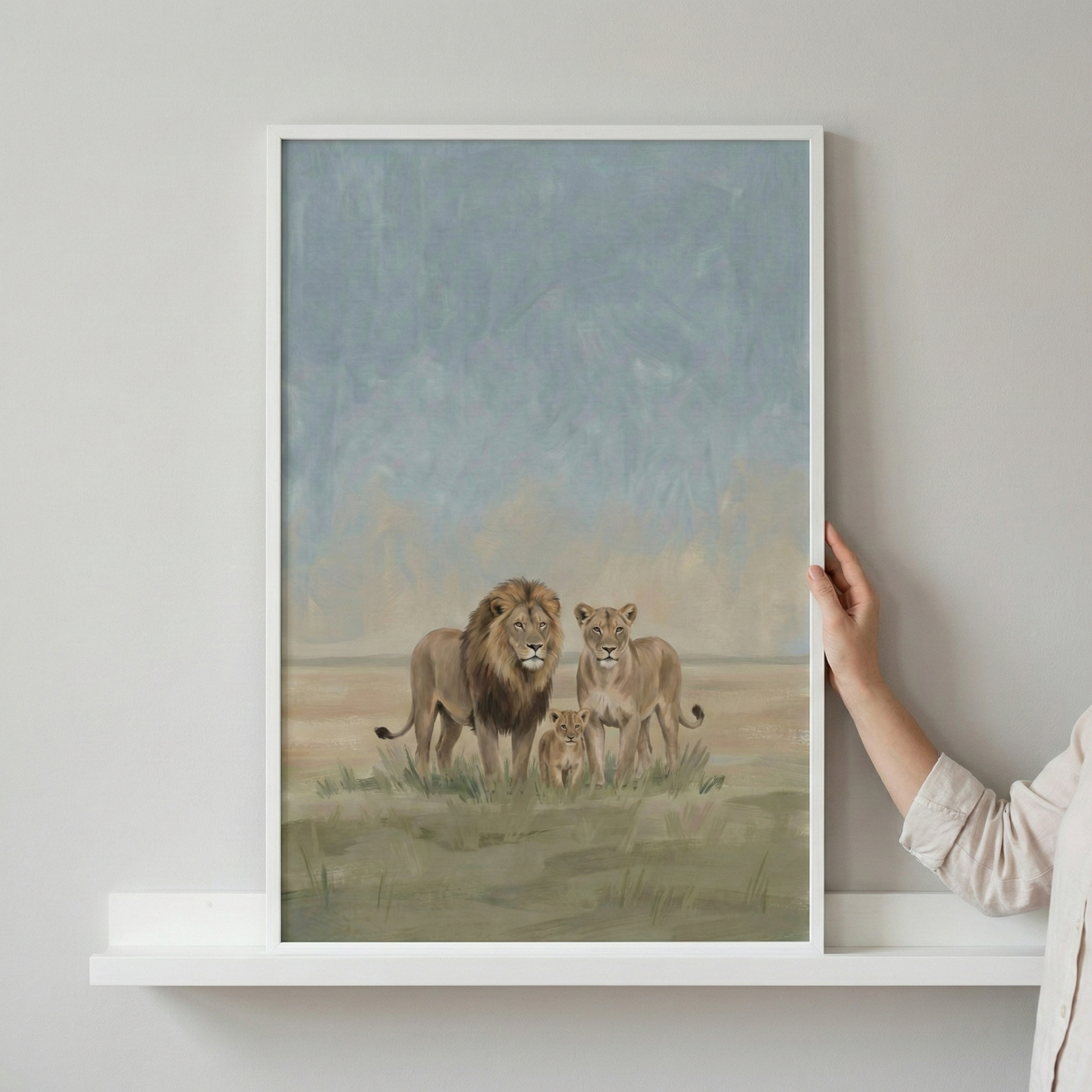A vertical framed artwork depicts a family of three lions standing in a grassy field. The illustration features a large male lion with a prominent mane, a female lion, and a small cub positioned between them. The background consists of soft, muted colors suggesting a hazy sky and a distant horizon. The style of the piece is artistic with visible textures and a gentle color palette of earth tones and pale blues. 