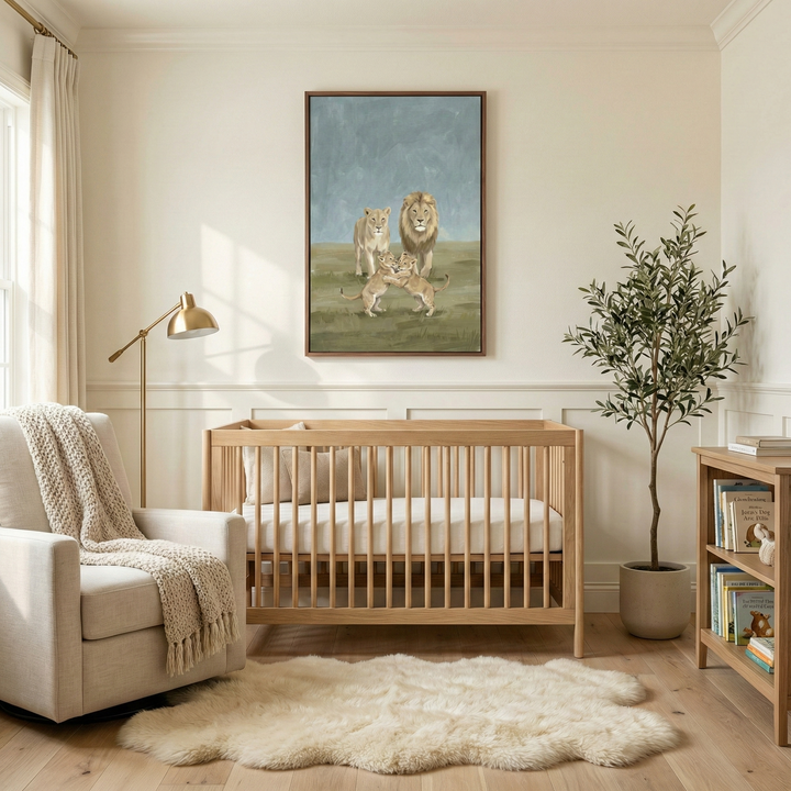 A serene nursery in neutral tones features light wood furniture and a warm, inviting atmosphere. On the wall hangs a large, framed vertical piece of canvas art showing a lion family—a male, a female, and two cubs playing—in a soft, muted landscape. Below the artwork is a matching light wood crib. To the left, a cream-colored upholstered armchair is accented by a heavy knit throw blanket, with a gold-finished floor lamp standing nearby. A plush, cream-colored faux fur rug lies on the light wood floor.
