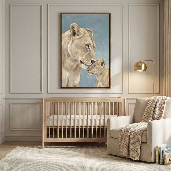 An illustrated canvas artwork featuring a mother lioness and her cub in a tender, nuzzling pose. The art has a soft, textured style with a muted blue background and is set in a thin wooden frame. It hangs on a wall with light-beige decorative paneling in a sophisticated nursery. Below the art is a light-wood crib. To the side, a beige armchair is adorned with a chunky knit throw. A gold, arched floor lamp provides warm light. The room is complete with a cream textured rug.