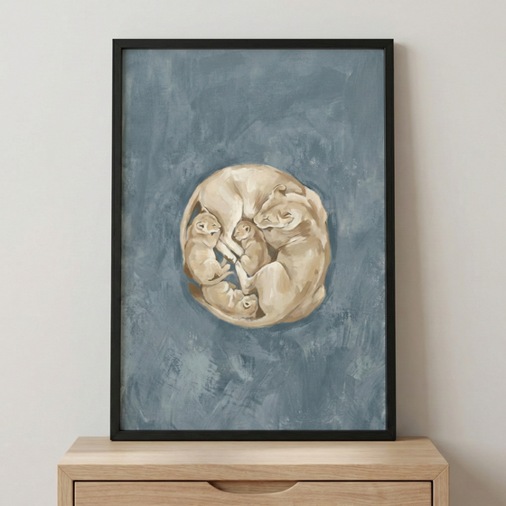 A vertical black-framed piece of art sits on a light wooden dresser. The artwork features a group of big cats curled together into a circular formation in the center. A larger tan lioness is nestled with three smaller cubs, all rendered with textured brushstrokes in shades of beige and cream. The background is a solid, muted blue with visible texture and variations in tone. The overall composition creates a sense of warmth and protection within the cool-toned surrounding space.