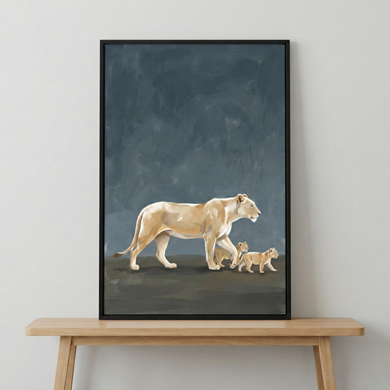 A vertical piece of wall art in a slim black frame sits on a light wood console table against a plain, light-colored wall. The artwork features a large female lion walking across a dark landscape, followed closely by two small cubs. The style of the art is expressive and minimalist, with visible brushstrokes and a palette of light cream and tan for the animals. The background of the art is a deep, textured navy blue that contrasts with the lighter subjects. 