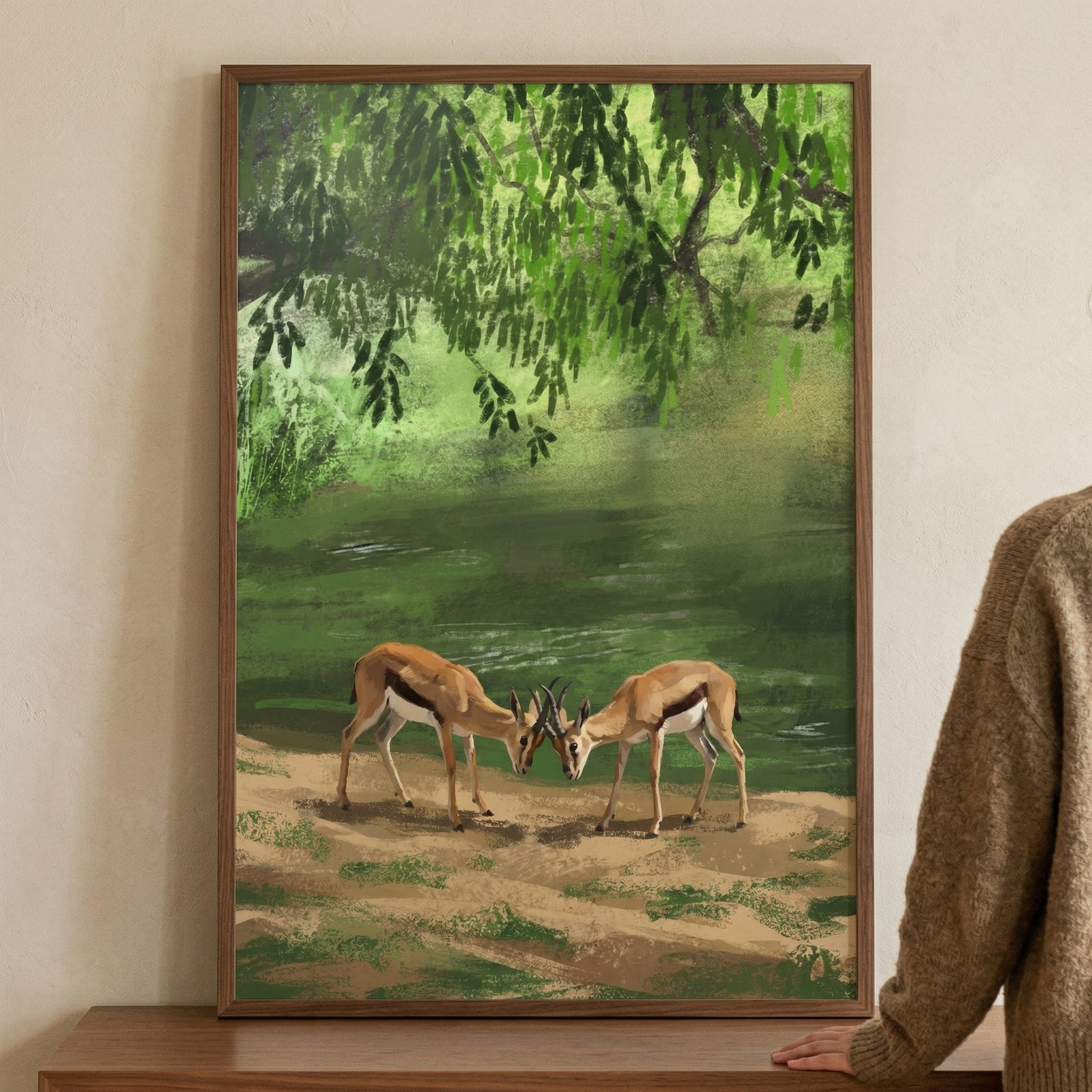A framed vertical illustration displays a tranquil nature scene. At the center, two slender antelopes with light brown coats and white underbellies stand on a dusty, earth-toned ground. 