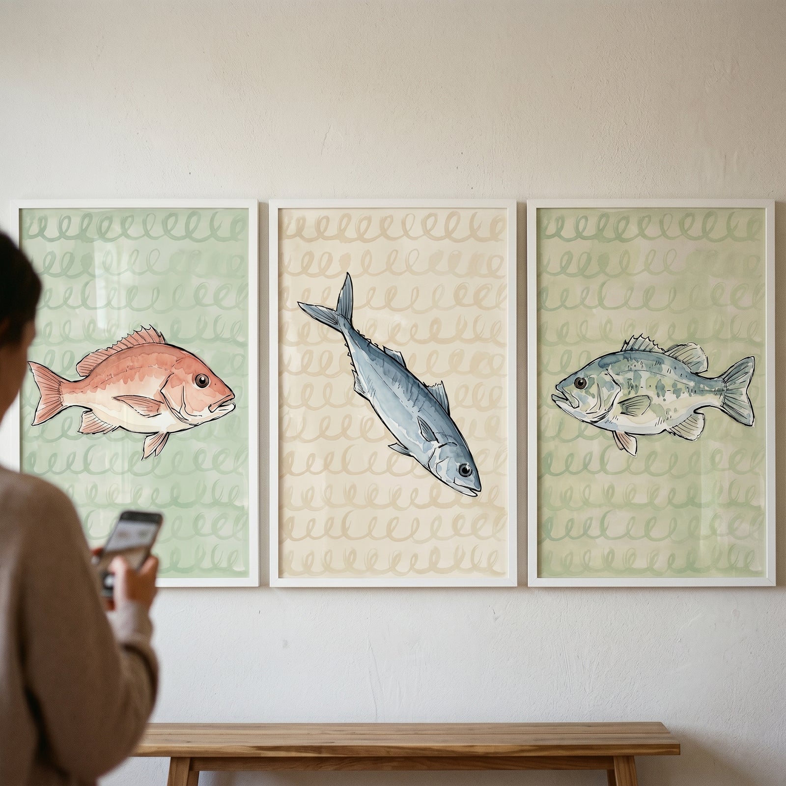A person takes a photo of a loopy scribble pattern fish wall art set of 3 hanging in frames above a wooden bench.