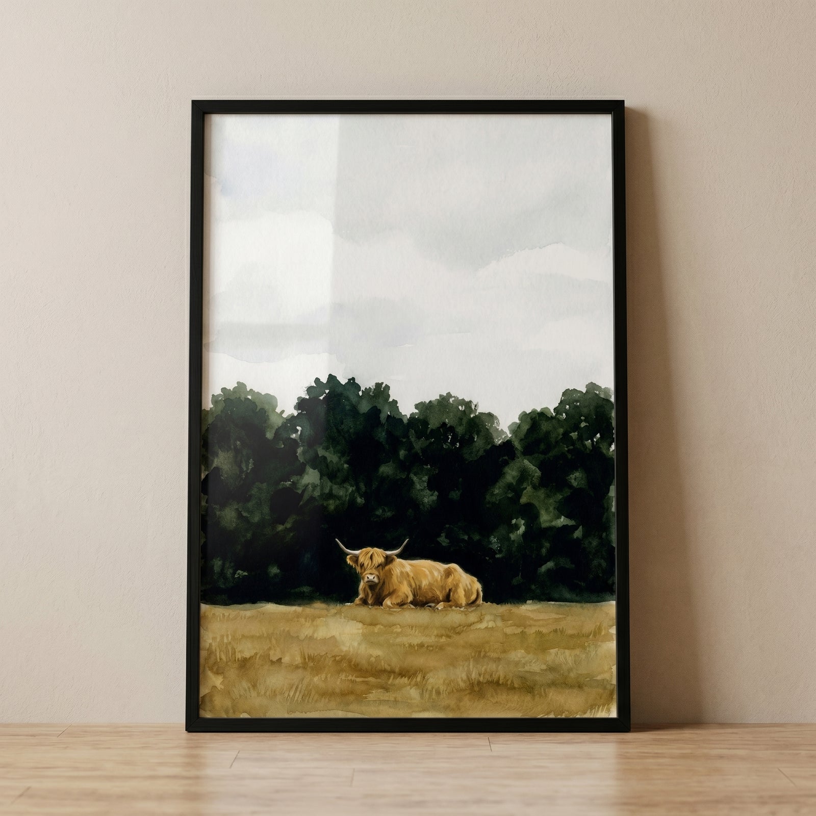 Framed watercolor lying down highland cow wall art resting in a tan field with dark forest trees and a cloudy sky.