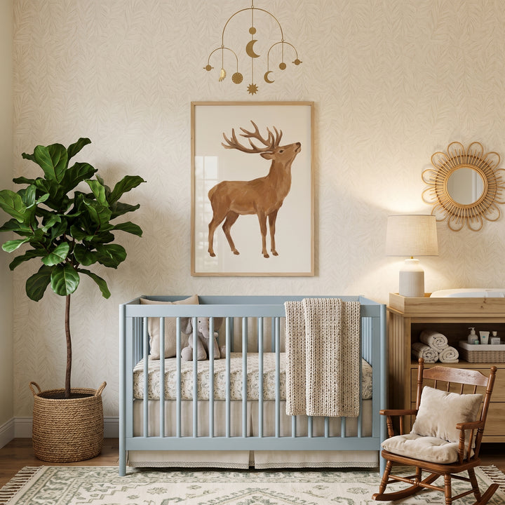Blue crib in a nursery with a tall plant and majestic large antlers stag wall art below a celestial mobile.