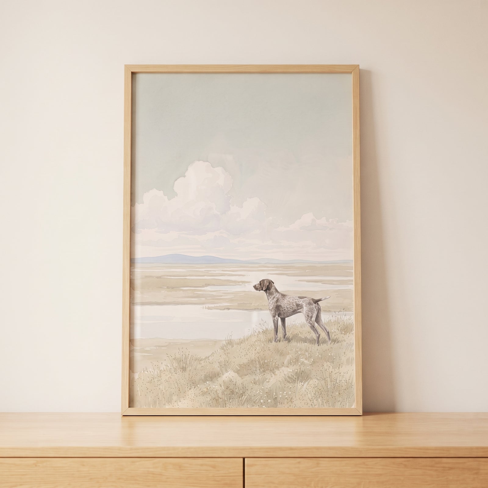 Marsh landscape shorthaired pointer dog wall art in a wood frame on a wooden cabinet against a neutral wall.