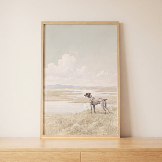 Marsh landscape shorthaired pointer dog wall art in a wood frame on a wooden cabinet against a neutral wall.